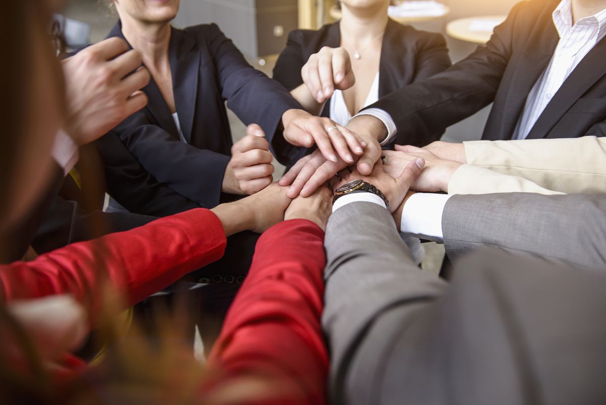 Over shoulder view of group of businesswomen and men with hands together in a circle